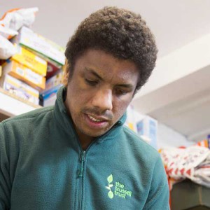 A male foodbank volunteer with shelves of food in the background