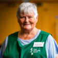 Food bank staff member looking at camera smiling with arm resting on pack of toilet paper