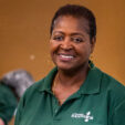 Food bank staff member looking at camera smiling with arm resting on pack of toilet paper