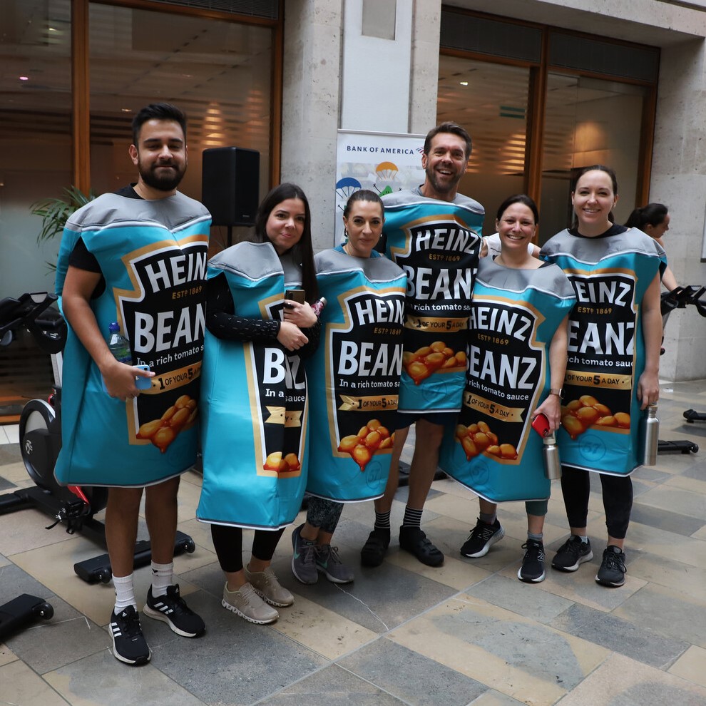 A group of six fundraisers stand in a line and smile towards the camera. They are all wearing baked bean tin costumes.