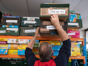A volunteer reaches up for a box on a shelf. The shelf is full of boxes of cereal.
