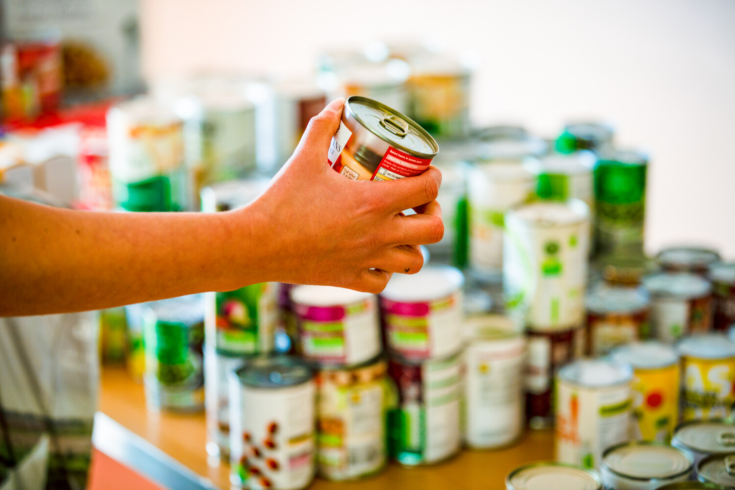 A hand holds a tinned food item. There are more tinned food items in the background.