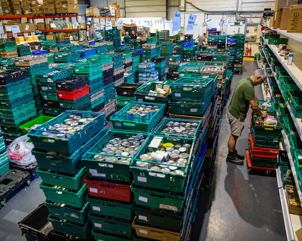 Food bank warehouse stacked with crates and a member of staff unpacking crates